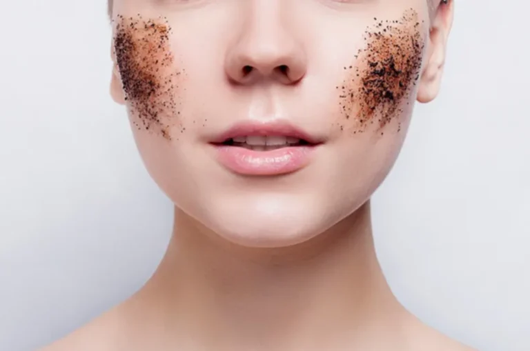 A person with coffee grounds applied as a facial scrub on both cheeks. The white background contrasts with the natural, exfoliating texture of the scrub.