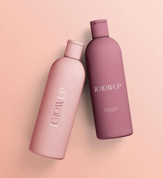 Two pink and mauve shampoo bottles labeled "GLOWUP" lie tilted on a pastel pink background, conveying elegance and modernity.