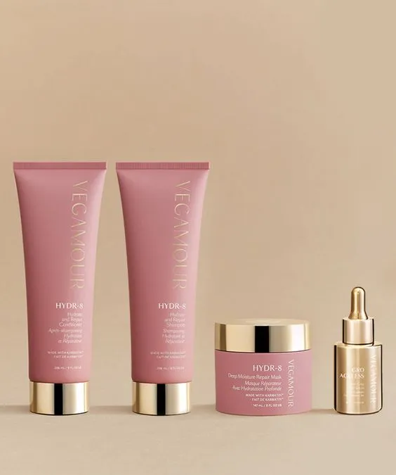 Luxurious hair care products on display: two pink tubes, a jar, and a gold dropper bottle with pink accents, set against a warm beige background.